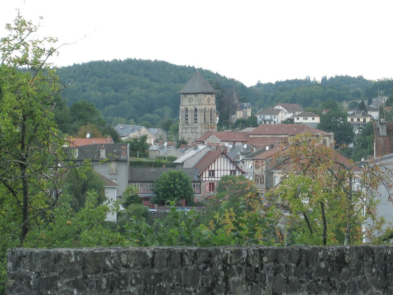 Vue sur le centre-bourg d'Eymoutiers, ses maisons anciennes et le clocher de la collégiale Saint-Étienne, au pied des collines boisées