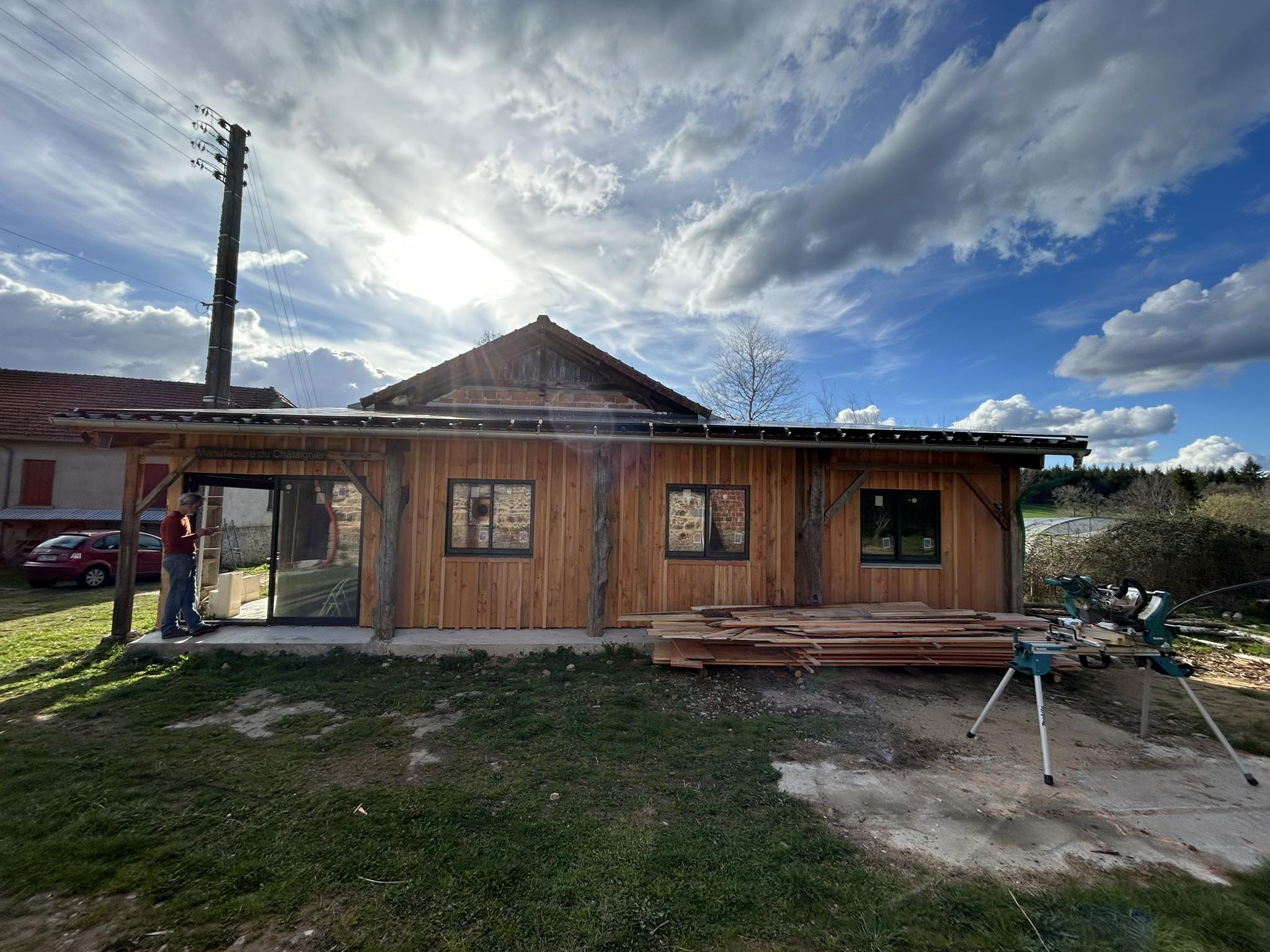 La Manufacture du Châtaignier à Chabaud : bâtiment en bardage bois avec son enseigne, piles de bois et scie à onglet
